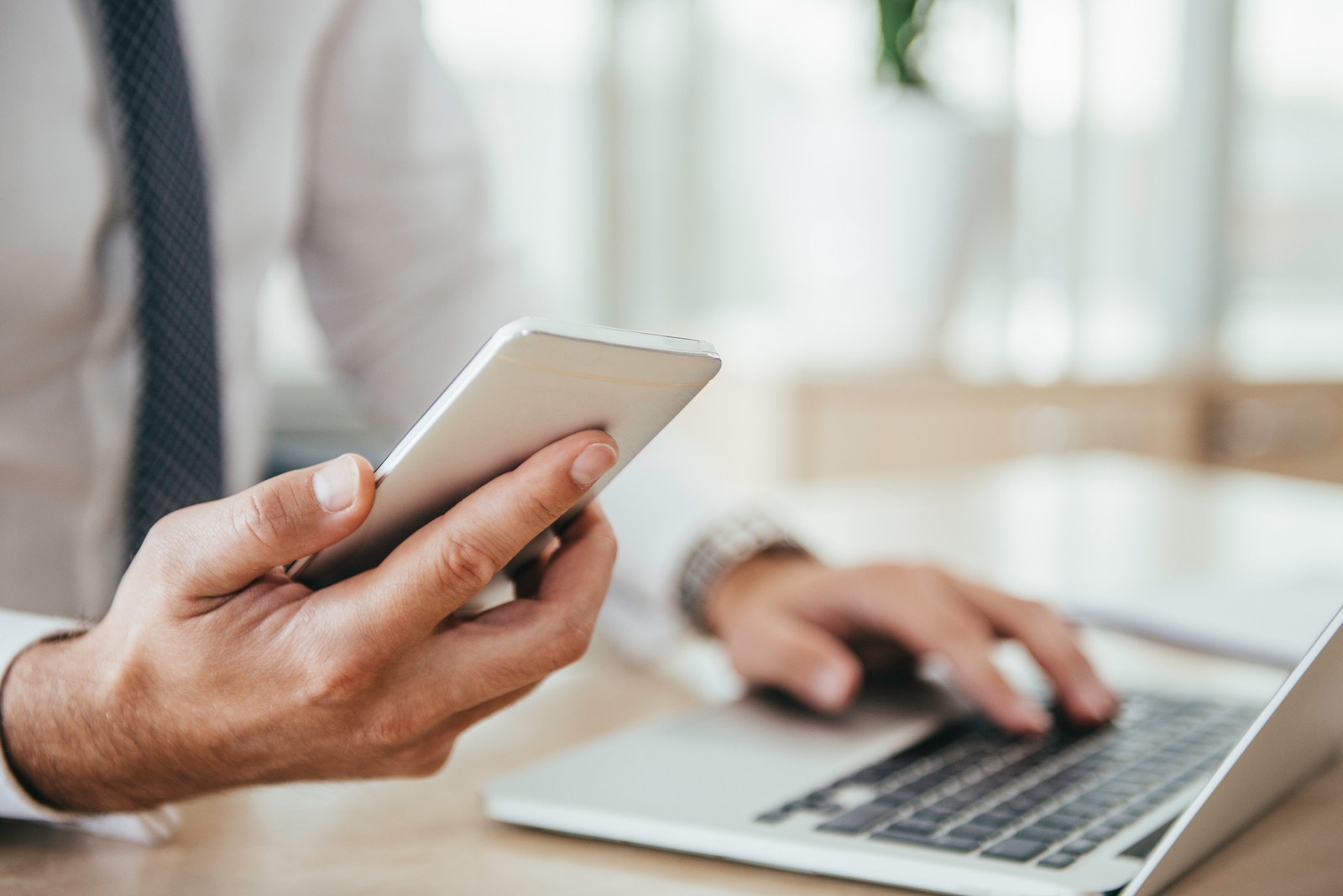 Midsection Of Businessman Using Laptop While Holding Mobile Phone On Table In Office